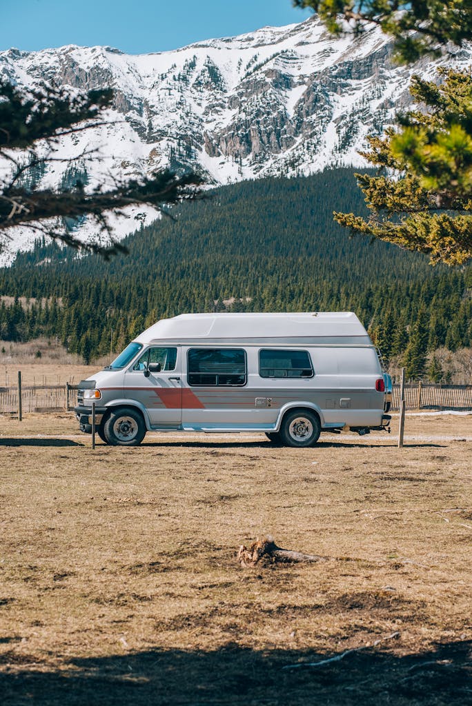 A camper van parked in a field with majestic snow-capped mountains, ideal for travel enthusiasts.