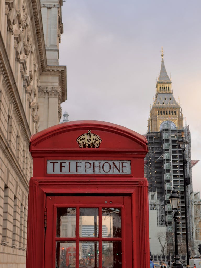 Classic red telephone booth in London with Big Ben and historic architecture.
