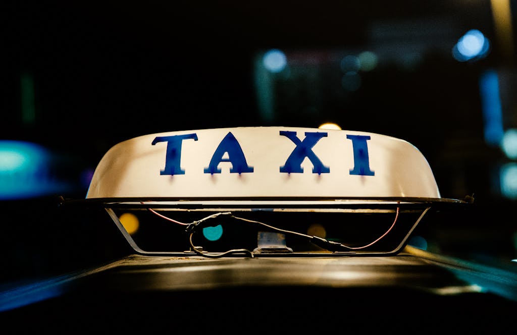 Photo by NEOSiAM 2024+ Close-up view of an illuminated taxi sign in a bustling city at night.